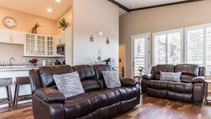Ein modernes Wohnzimmer mit zwei Ledersofas, einer Küche im Hintergrund und großen Fenstern.