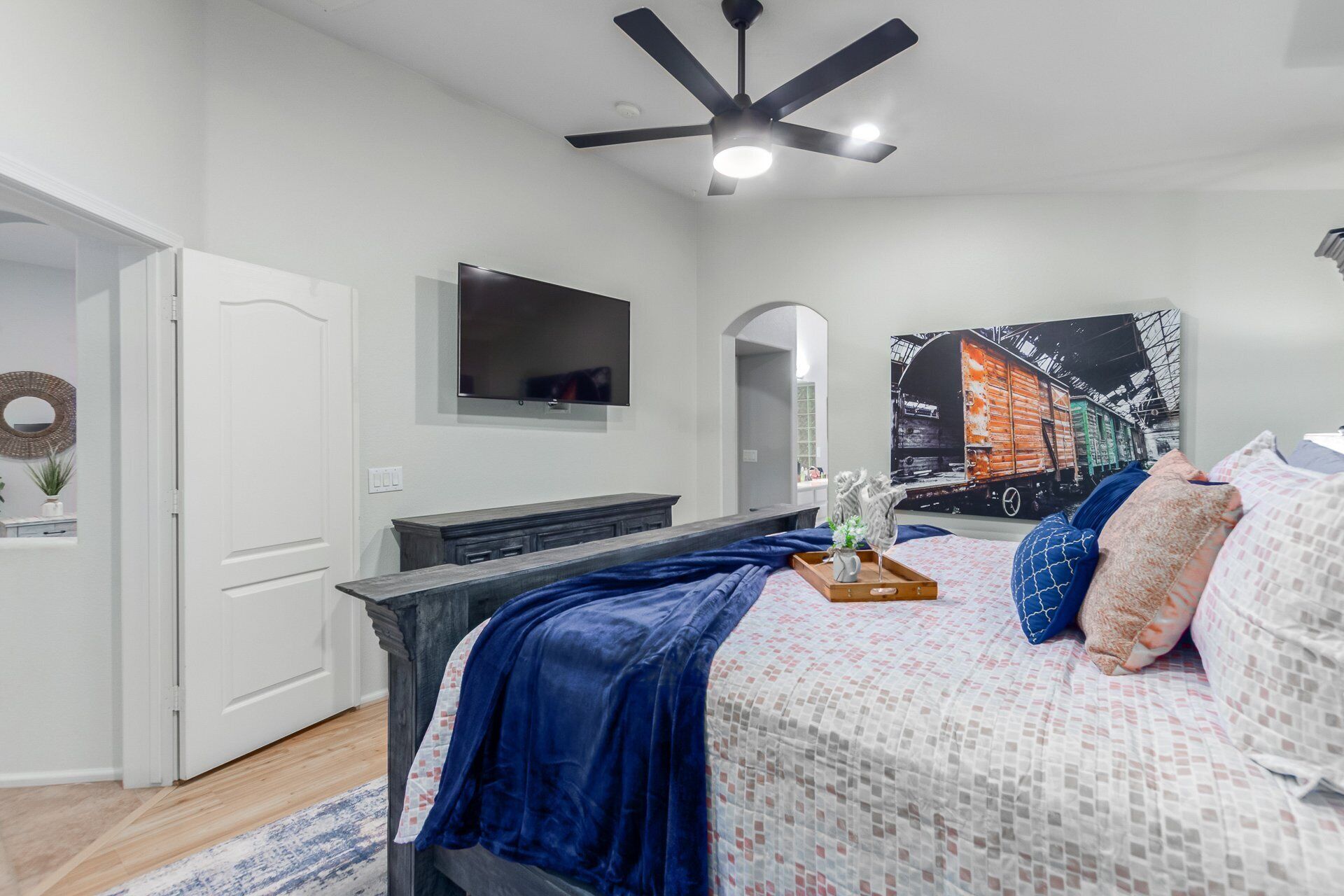 A bedroom with a bed, a dresser, a TV, and a ceiling fan.