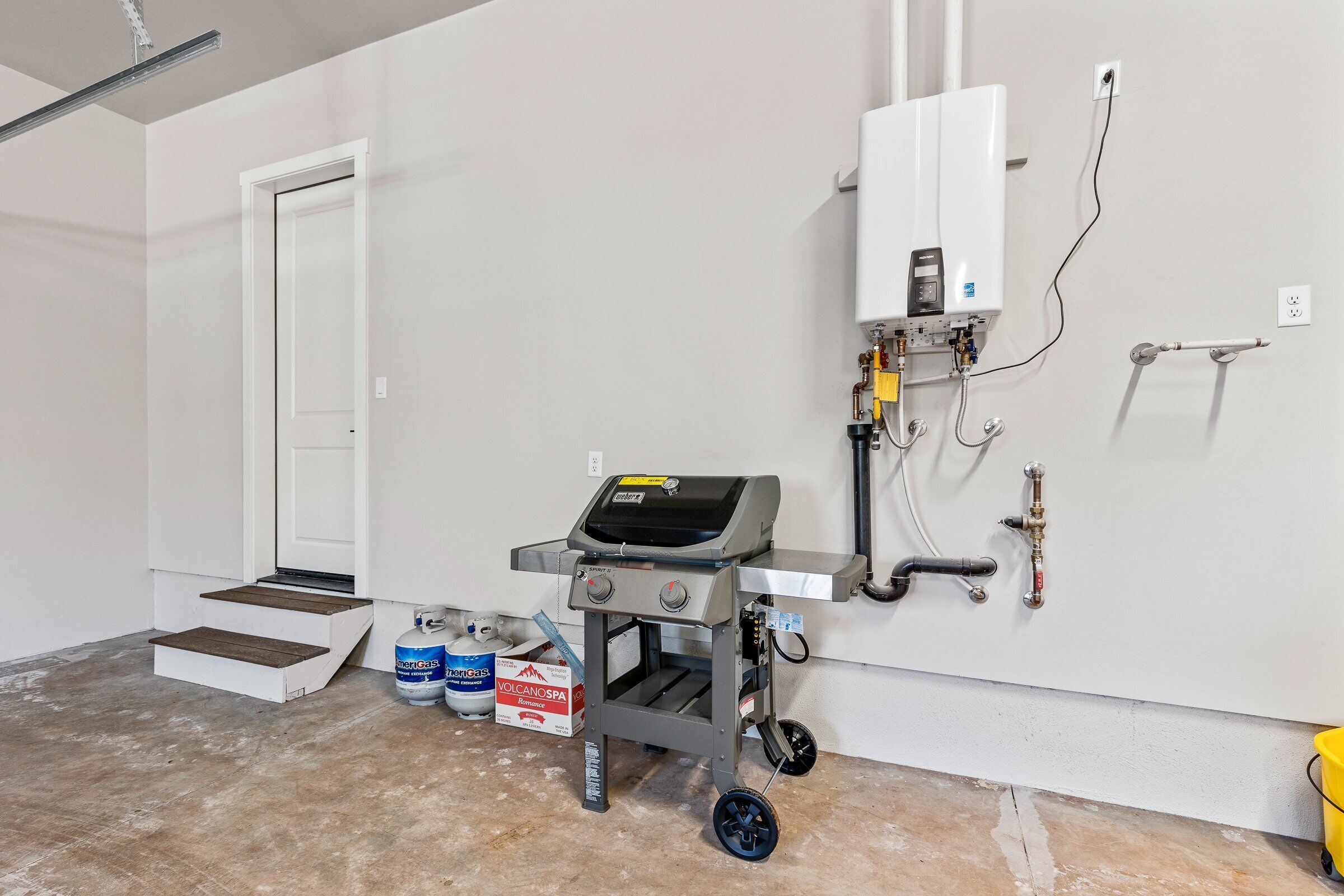 A room with a portable gas grill, a water heater, and a step leading to a door.