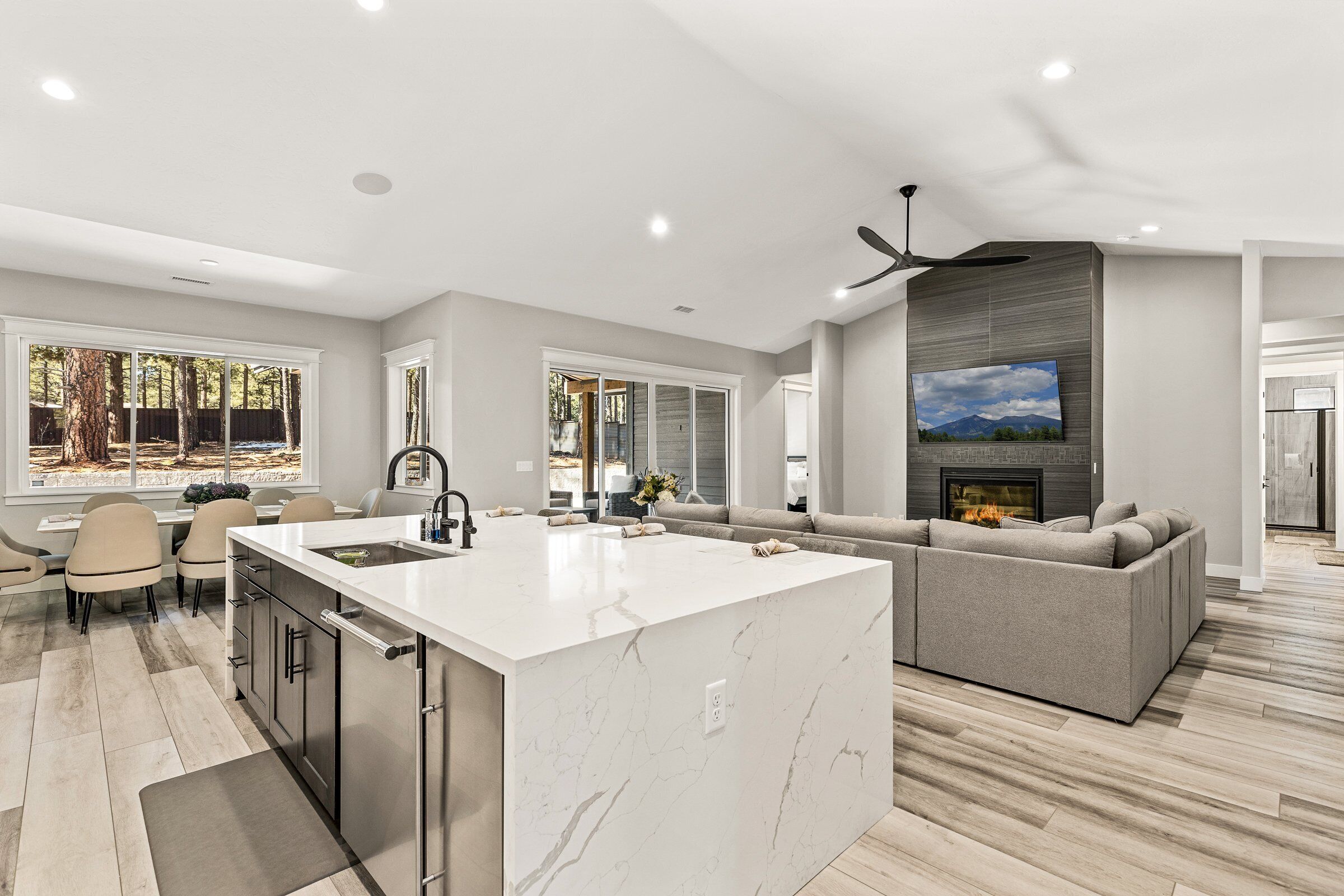 A modern kitchen with a large island, a dining area with chairs, and a living room with a sofa and fireplace.