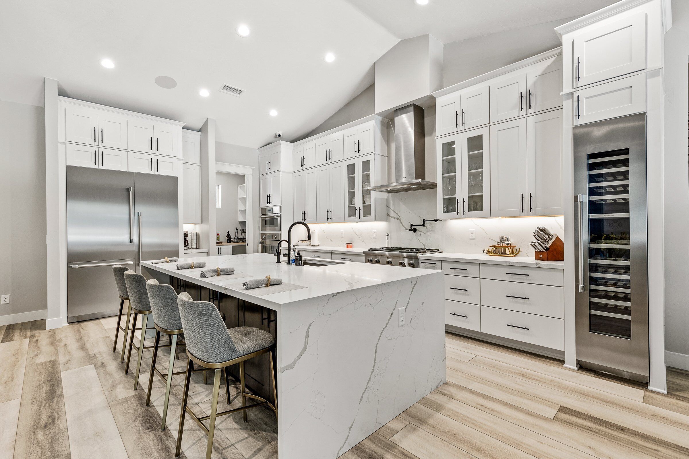 A modern kitchen with white cabinetry, a large island with bar stools, stainless steel appliances, and a wine cooler.