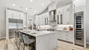 A modern kitchen with white cabinetry, a large island with bar stools, stainless steel appliances, and a wine cooler.