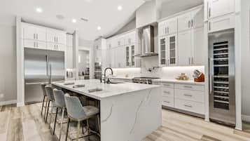 A modern kitchen with white cabinetry, a large island with bar stools, stainless steel appliances, and a wine cooler.