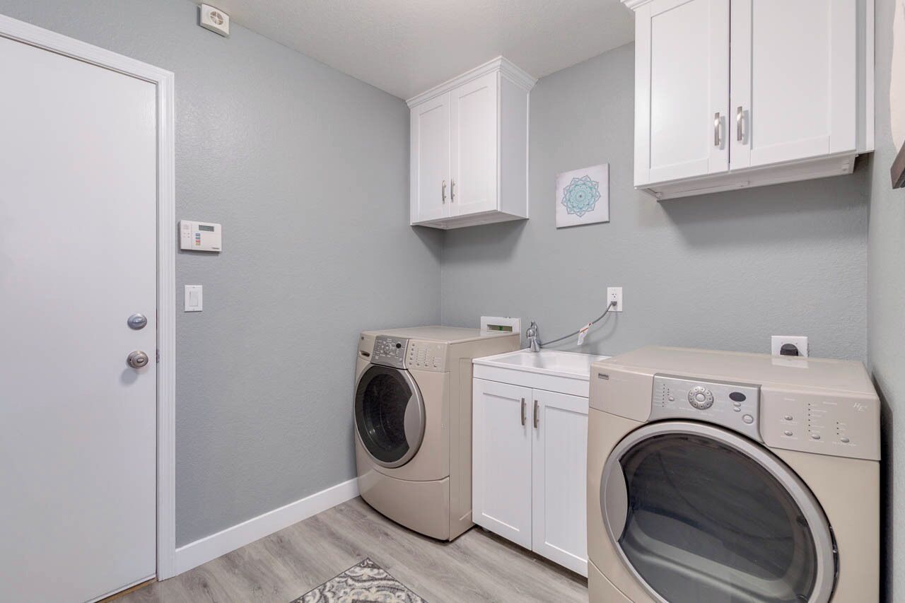 A laundry room with two washing machines, a sink, and white cabinets.