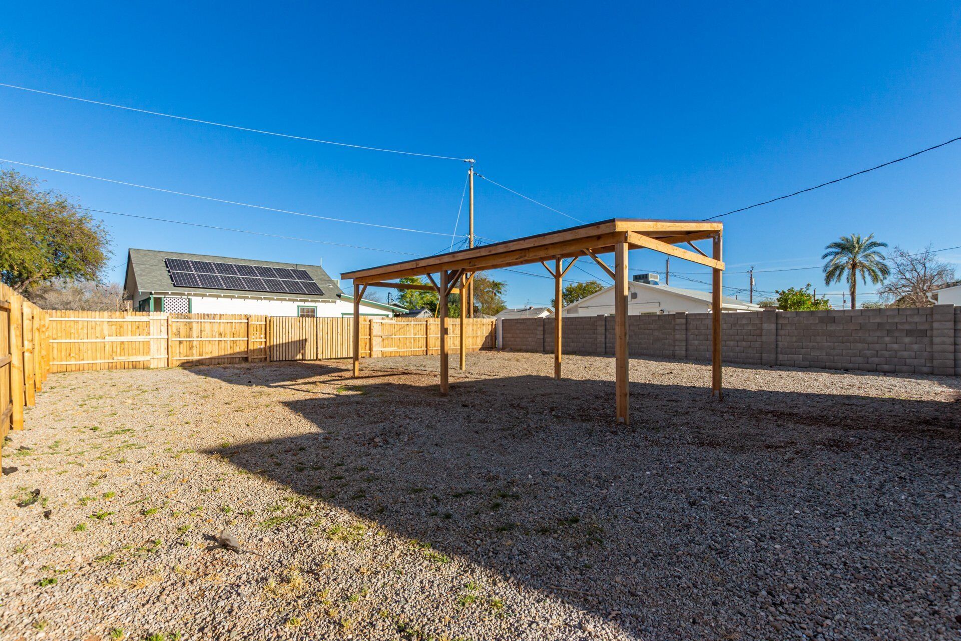 A backyard with a wooden pergola, a fenced area, and a house with solar panels.