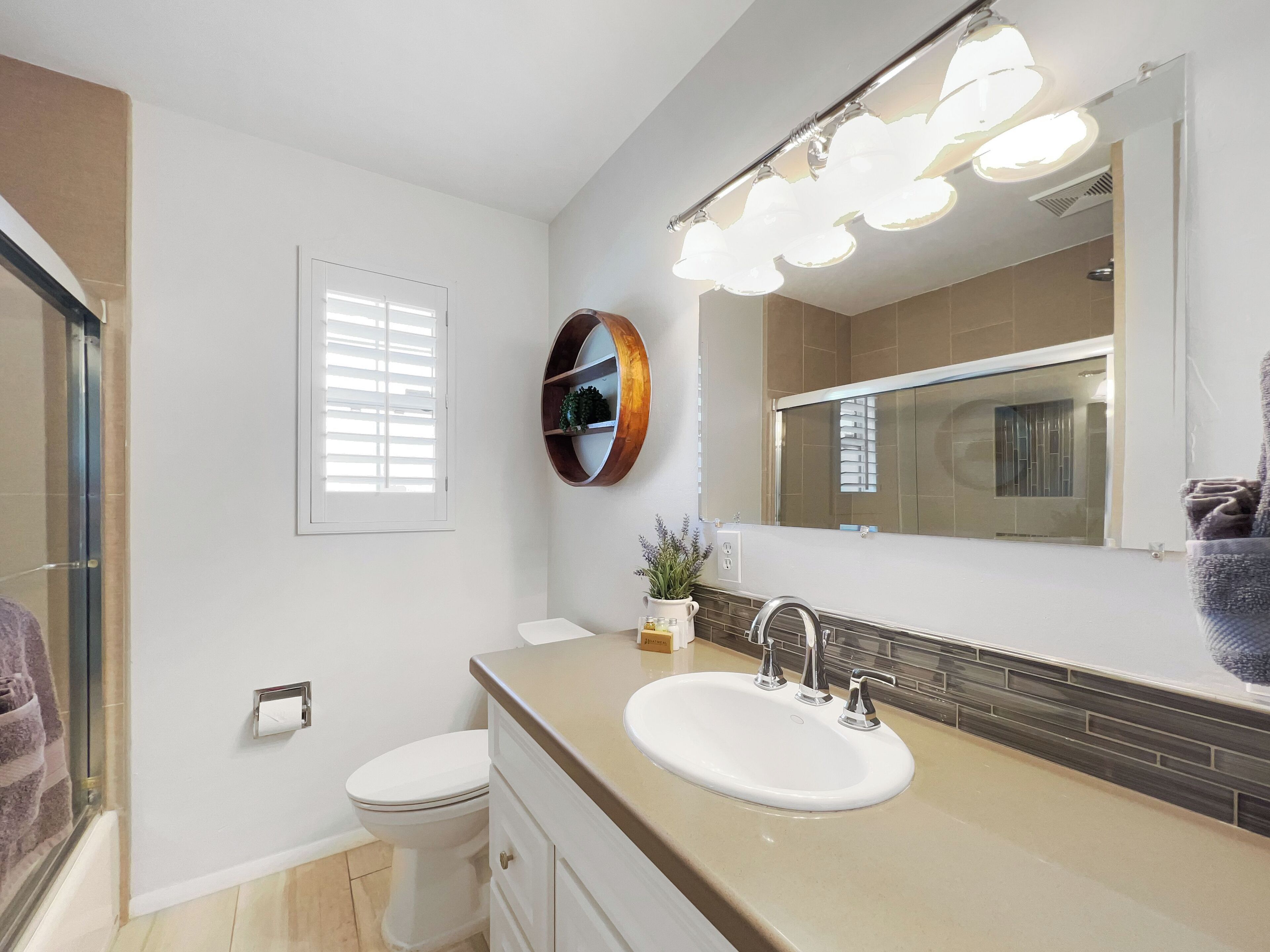 A bathroom with a white sink, a mirror, and a toilet. There is a towel rack and a potted plant on the counter.