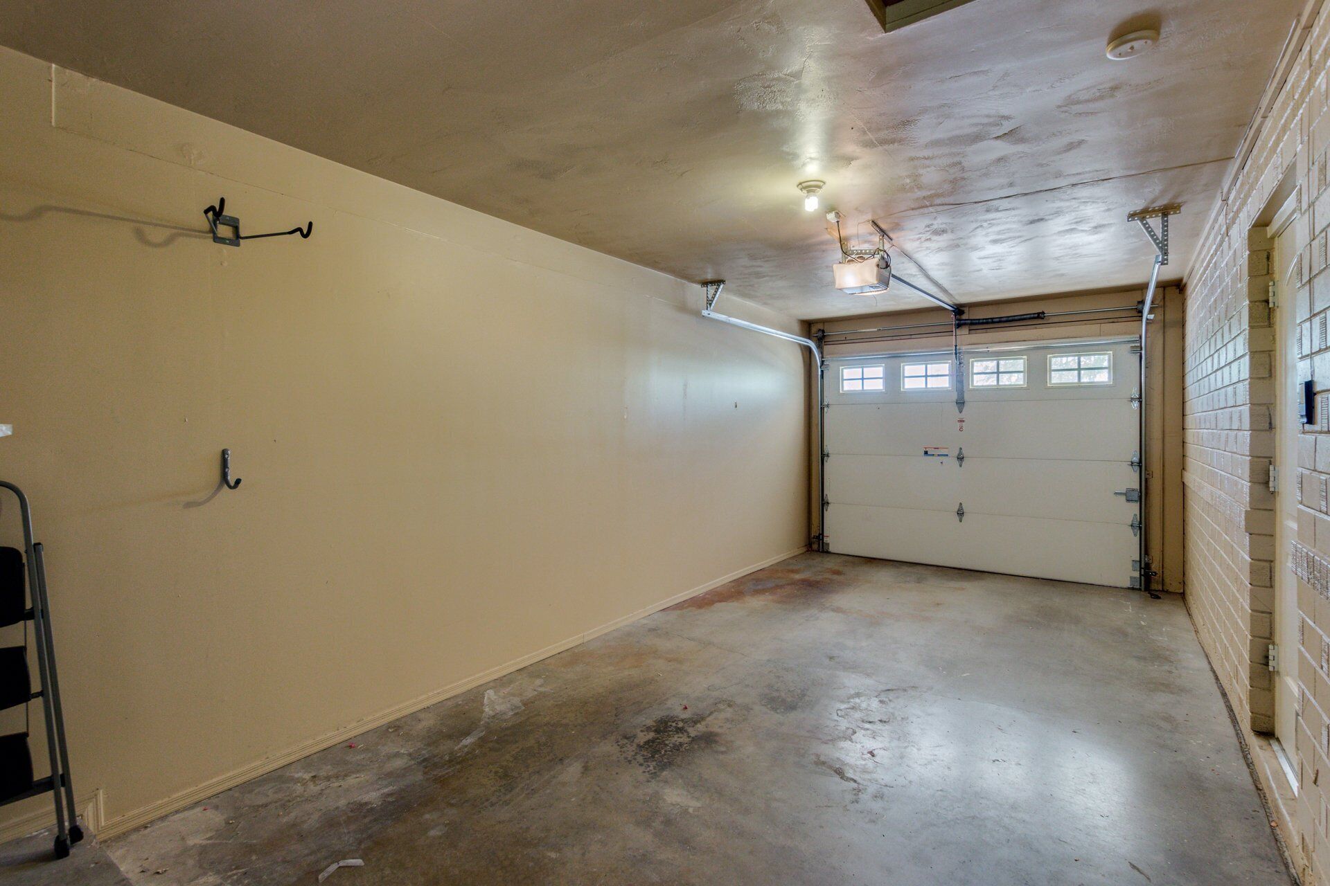 A garage with a concrete floor, a white door, and a metal ladder.
