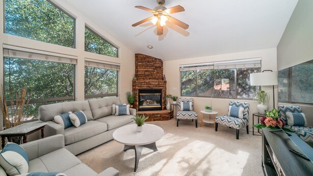 A spacious living room with a fireplace, large windows, and a ceiling fan. - Lookout Payson (Payson)