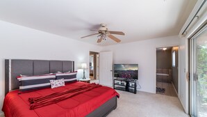 Ein Schlafzimmer mit einem großen Bett, einem Deckenventilator, einem Fernseher und einer Glastür zu einem Balkon.