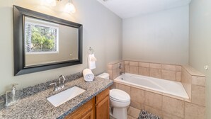 Ein modernes Badezimmer mit einer Granittheke, einem Doppelwaschbecken, einer Toilette und einer Badewanne.