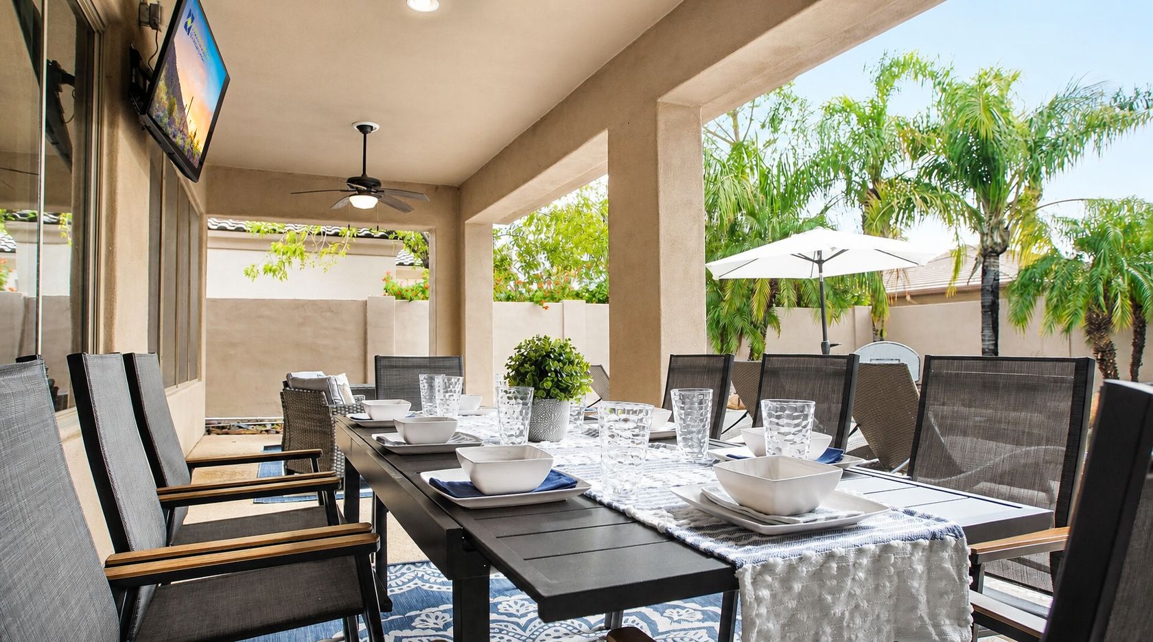 An outdoor dining area with a table set for four, surrounded by chairs, and a ceiling fan above.