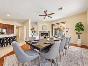Un espace repas avec une longue table, des chaises à revêtement gris et un ventilateur de plafond.