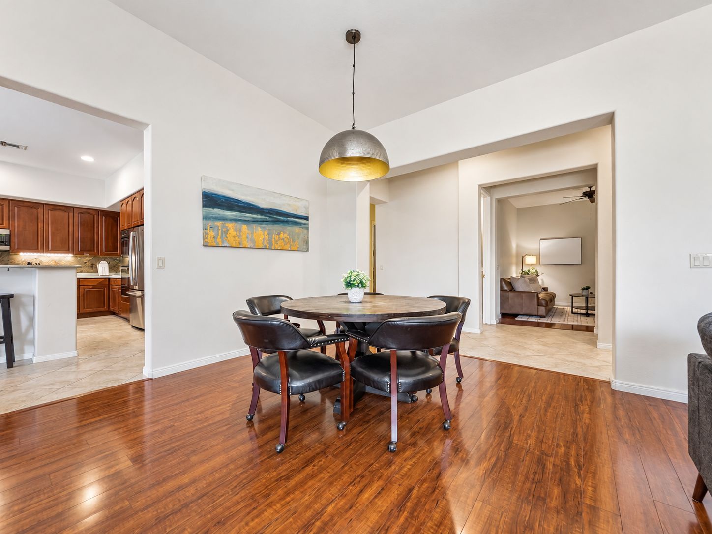 A modern kitchen with wooden cabinets, a stainless steel refrigerator, and a dining area with a round table and chairs.