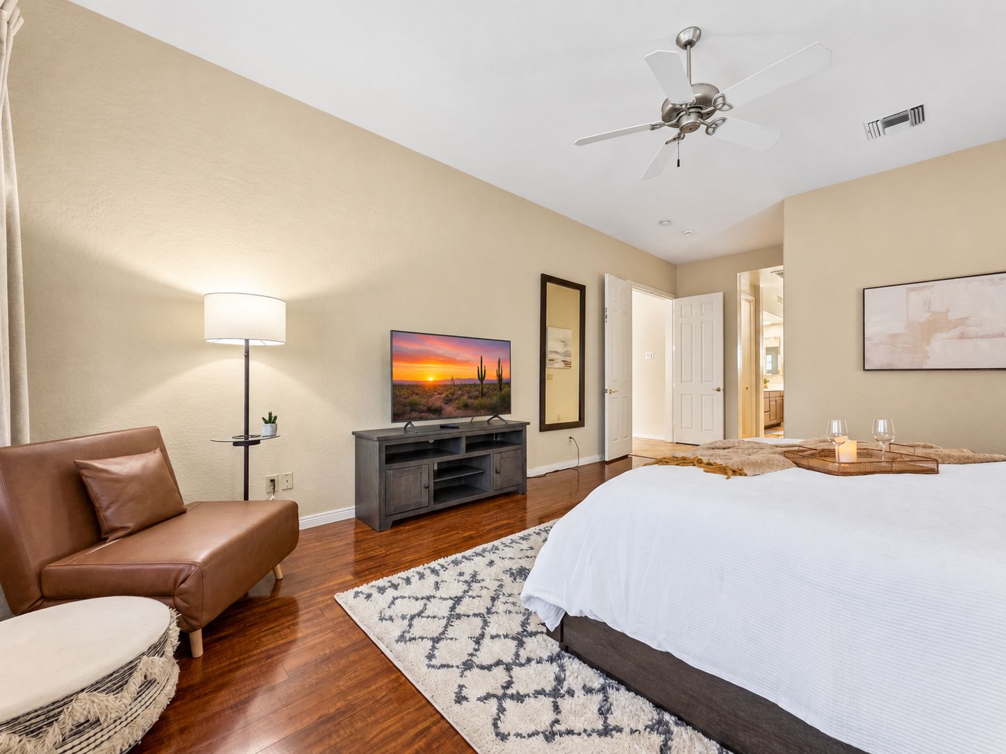 A hotel room with a bed, a seating area with a chair, a television, a ceiling fan, and a door leading to another room.