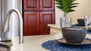A modern kitchen with wooden cabinets, stainless steel appliances, and a blue woven placemat. - Lynx Chandler/ocotillo (Chandler)
