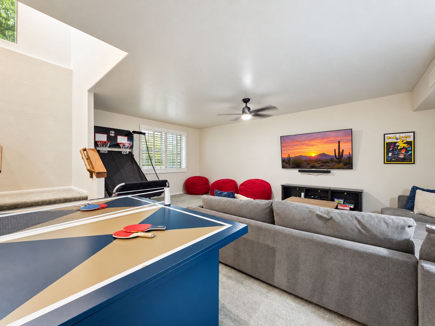 A living room with a ping pong table, a couch, a TV, and a ceiling fan.