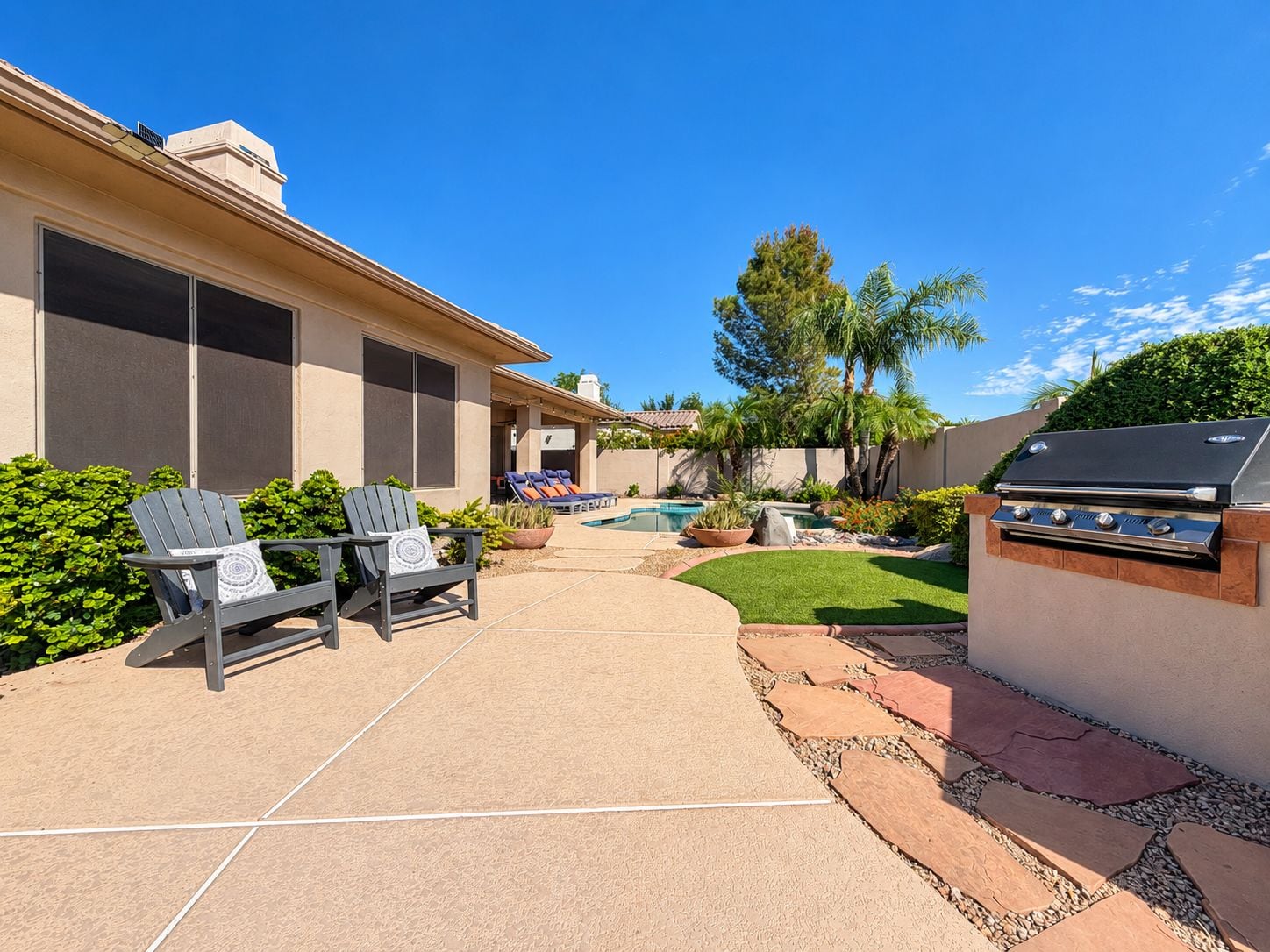A backyard with a barbecue grill, lounge chairs, a swimming pool, and a well-maintained lawn.