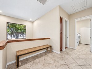 A hallway with a bench, a door leading to a laundry room, and a window with a view of trees. - Lynx Chandler/ocotillo (Chandler)