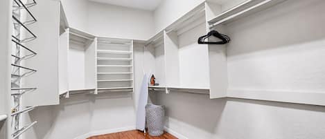A walk-in closet with shelves, a hanging rack, and a trash bin.