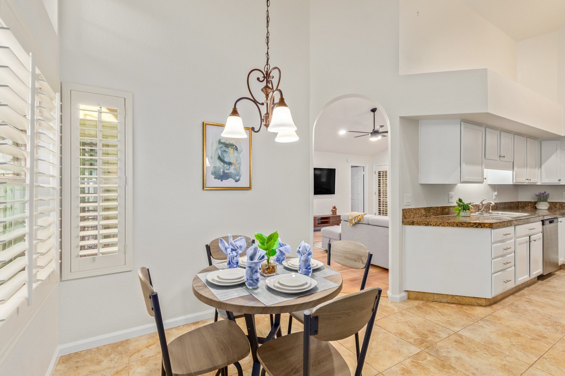 A dining area with a round table set for four, a chandelier, and a painting on the wall.
