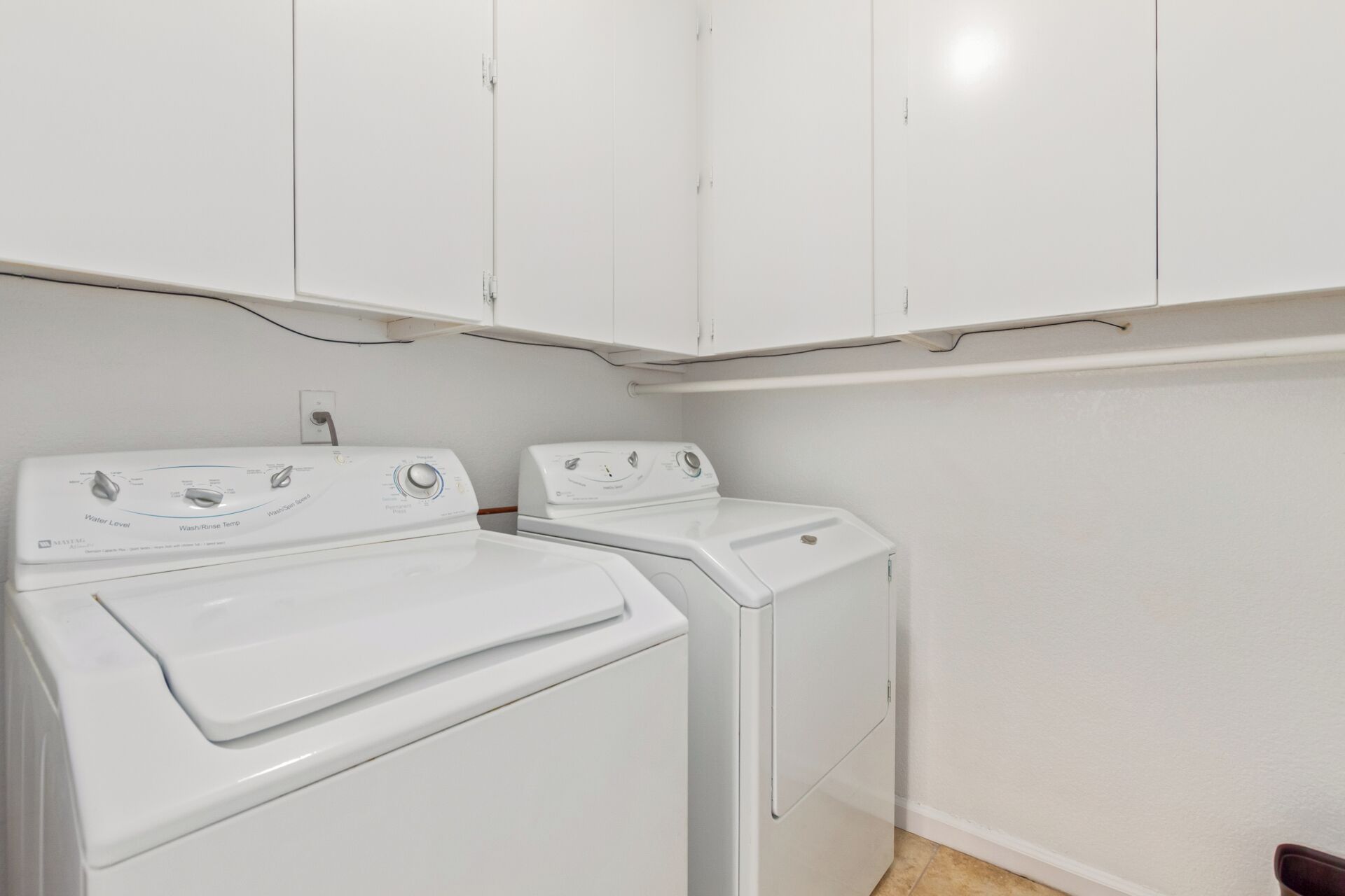 A laundry room with two white front-loading washing machines and a white cabinet above them.