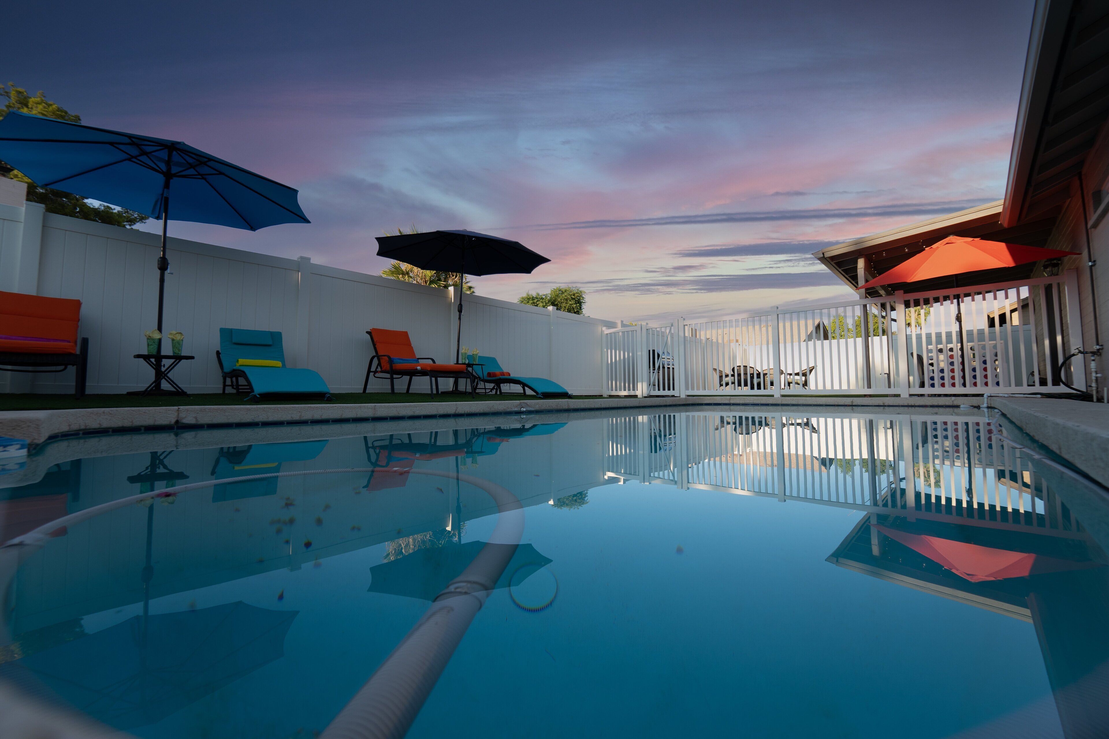 A swimming pool with lounge chairs and umbrellas, surrounded by a white fence.