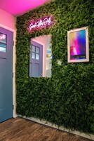 A wall with a neon sign, a framed picture, and a door.