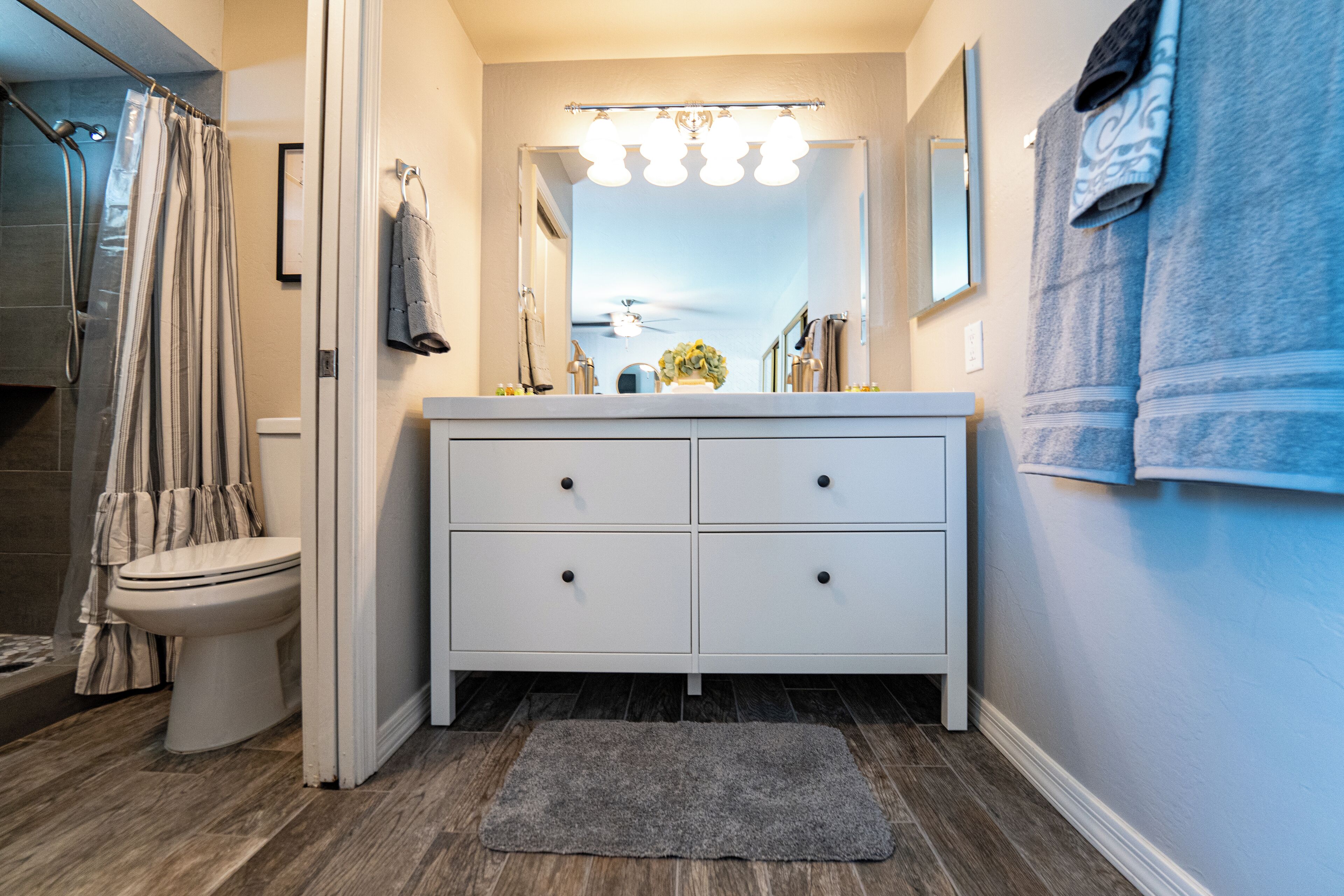 A bathroom with a white vanity, a shower curtain, a toilet, and a mirror with lights.