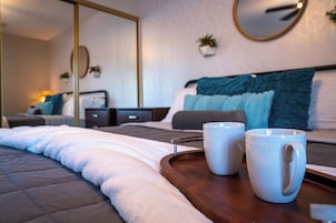 Una cama bien tendida con un edredón blanco y una bandeja de madera con dos tazas blancas.