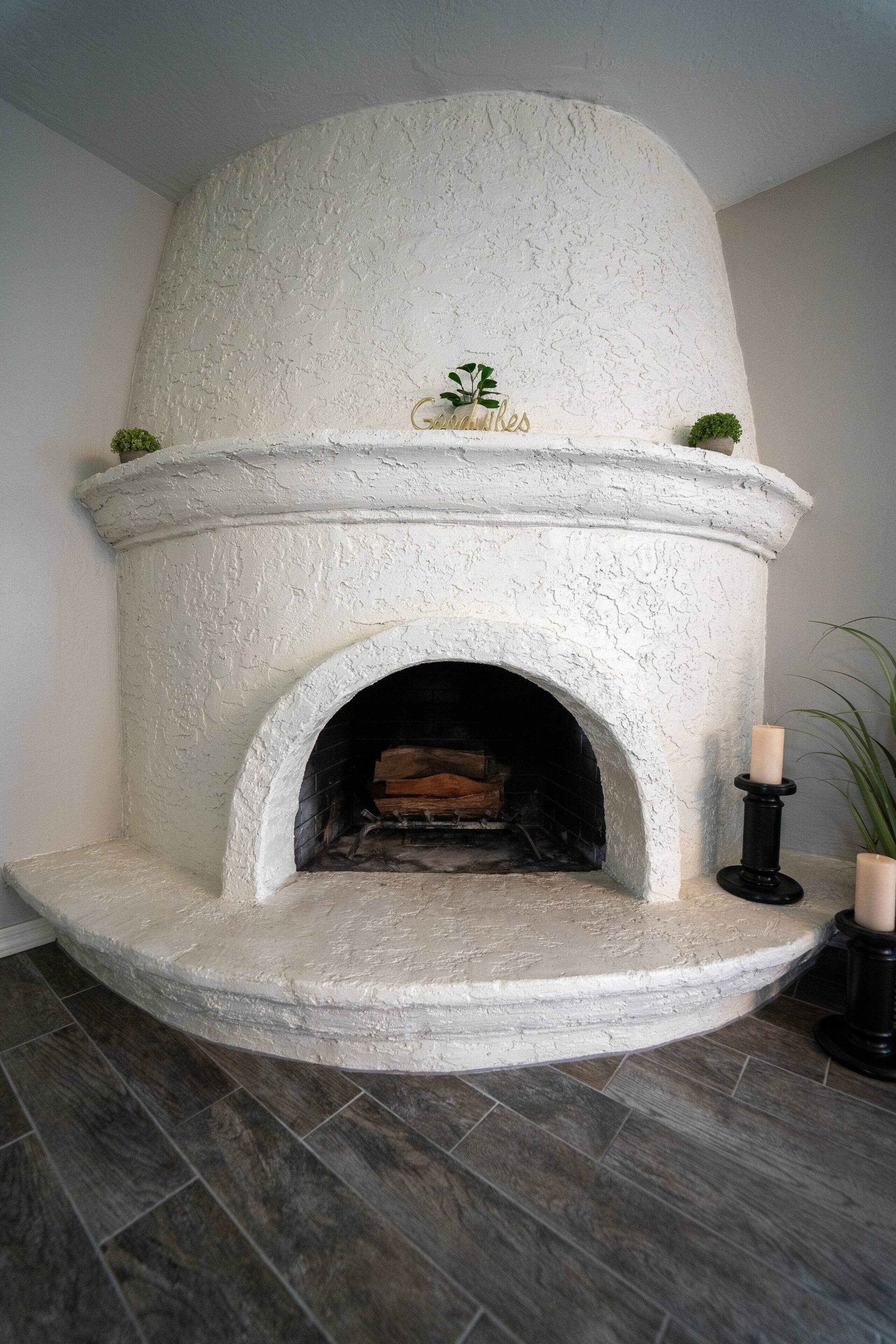 A white stone fireplace with a decorative sign, two candles, and a small plant on top.
