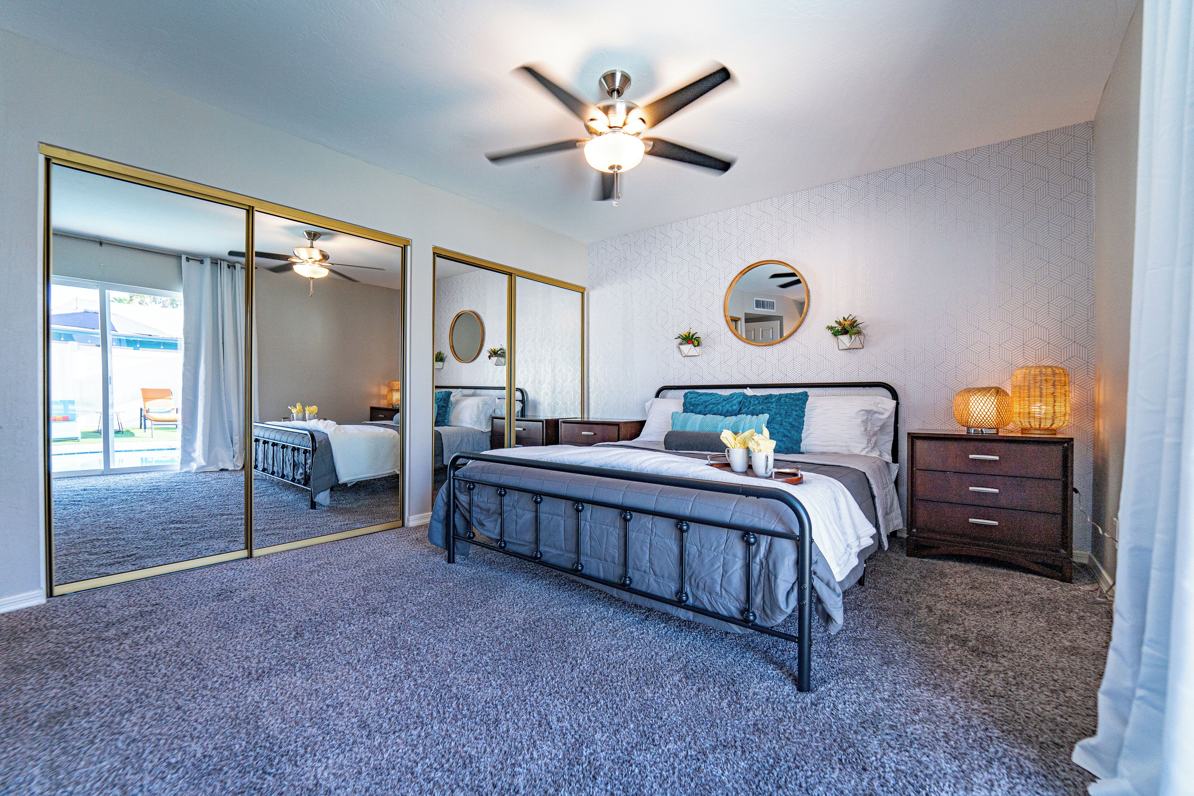 A bedroom with a large bed, a ceiling fan, a mirror, and a nightstand.