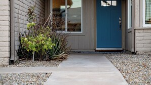 Ein Haus mit einer blauen Tür, einem Betonweg und einem kleinen Garten mit Pflanzen und Steinen.