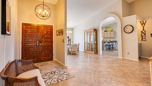 Un pasillo amplio con puerta de madera, un comedor y una cocina visibles a través de un arco.