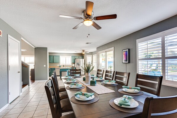 A dining area with a long table set for six, a ceiling fan, and a view of the kitchen in the background. - Ocotillo Glendale (Glendale)
