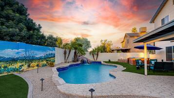 Un jardín con piscina, un patio con mobiliario exterior y un mural en la pared.
