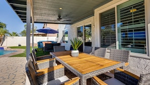 A covered patio with a wooden table and wicker chairs, a pool, and a view of a house. - Ocotillo Glendale (Glendale)