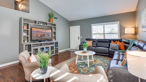 A living room with a television, seating, a coffee table, and a door. - Ocotillo Glendale (Glendale)