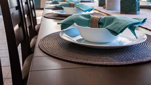 A dining table set with white plates, teal napkins, and a woven placemat. - Ocotillo Glendale (Glendale)
