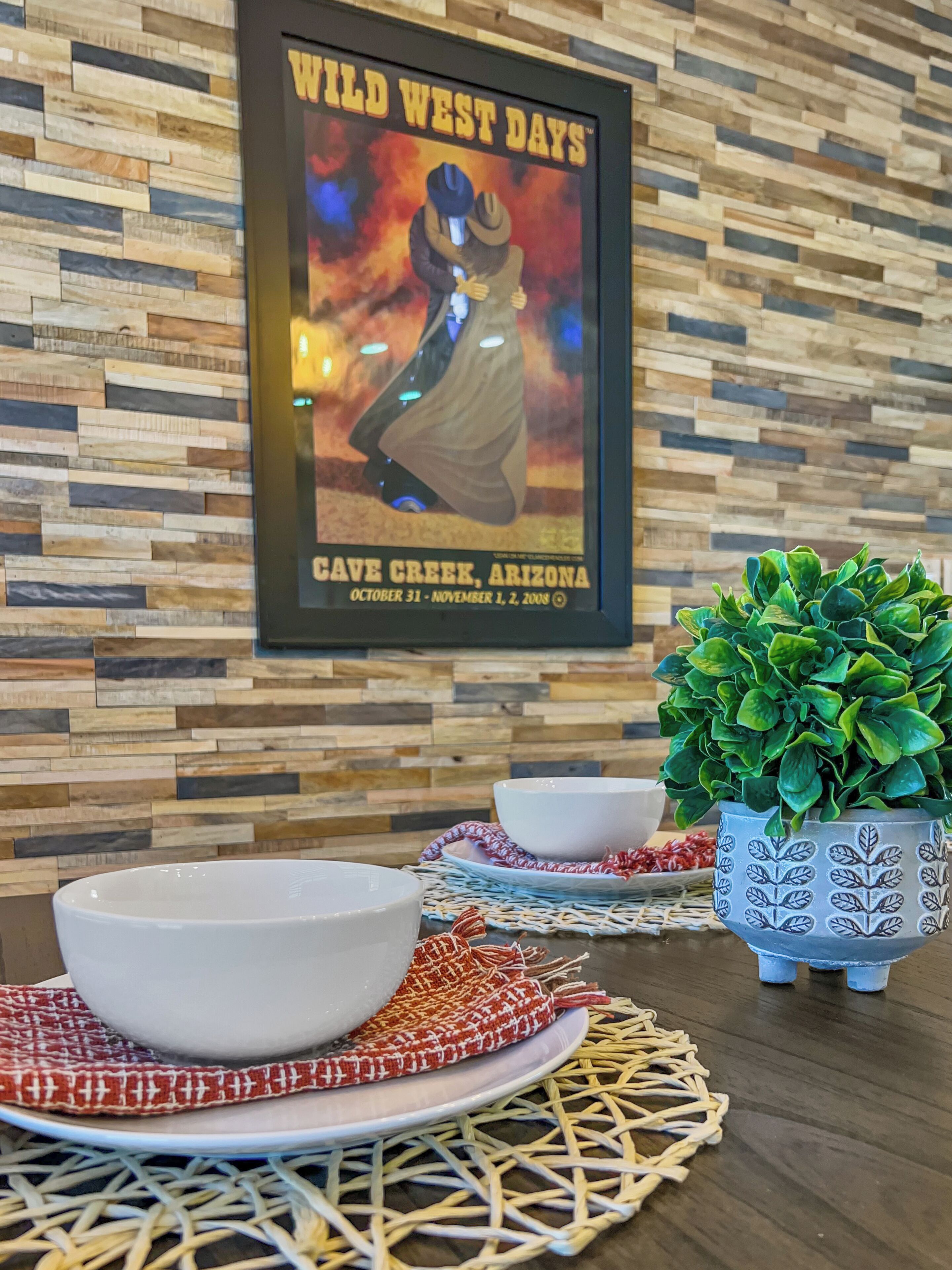 A framed poster of a cowboy on a horse, a potted plant, and a table with a bowl and a plate.