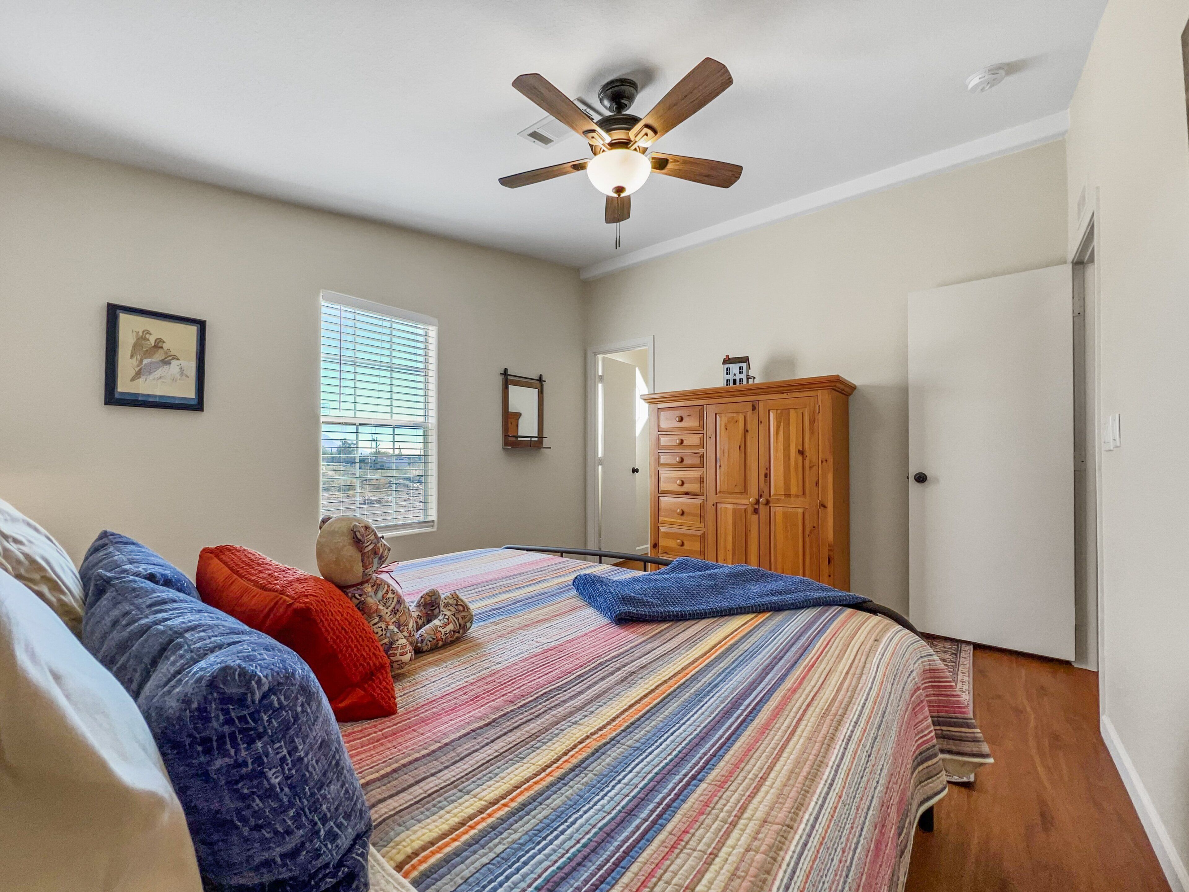 Une chambre à coucher comprenant un lit, un ventilateur de plafond, une fenêtre, une armoire et une porte.