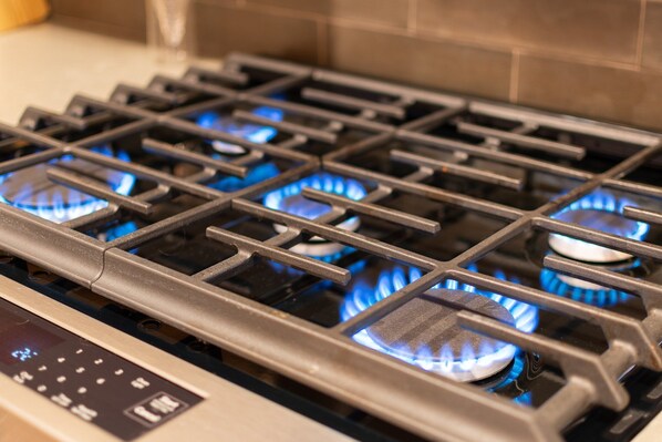 A gas stove with four burners, each with a blue flame, and a control panel with buttons. - Ruin Hill Kokopeli Pine (Pine)