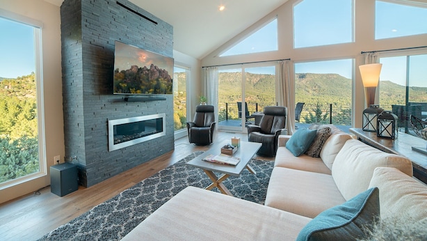 A spacious living room with a stone fireplace, comfortable seating, and large windows offering a view of the hills. - Ruin Hill Kokopeli Pine (Pine)