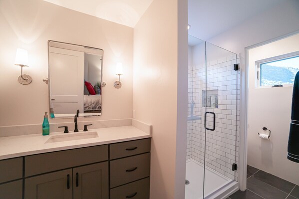 A modern bathroom with a glass shower, a sink with a mirror, and a window providing a view of the outdoors. - Ruin Hill Kokopeli Pine (Pine)