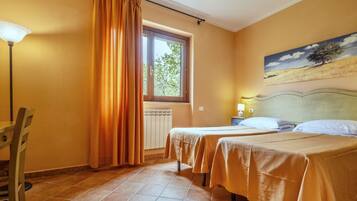 Une chambre d’hôtel avec deux lits, une fenêtre avec des rideaux, un radiateur, un tableau au mur et une lampe.
