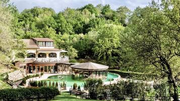 Une grande maison avec une piscine, entourée d’une végétation luxuriante et d’arbres.
