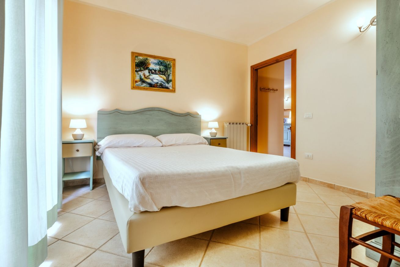 Ein Schlafzimmer mit einem Bett, Nachttischlampen, einem Bild an der Wand und einer Tür zu einem anderen Raum.