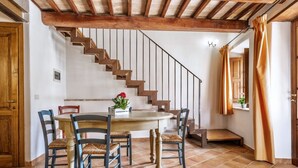 Un comedor con una mesa y sillas de madera, una escalera y un ventanal con cortinas.