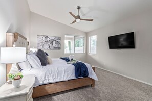 Quarto com cama, ventoinha no teto, televisão e janela com persianas.