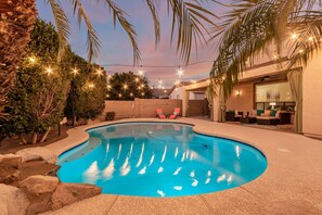 A swimming pool with a curved edge, surrounded by rocks and palm trees. There are lounge chairs and a covered seating area with a table and chairs. - Merino Mesa (Mesa)
