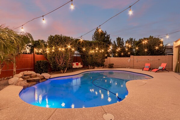 A swimming pool with a curved edge, surrounded by a brick wall and a wooden deck. There are lounge chairs and a small waterfall feature. - Merino Mesa (Mesa)